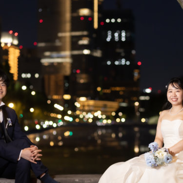 石造りのアーチの下に並んで腰かける新郎新婦。ビル群の夜景を背にした東京駅周辺のロケーションフォト