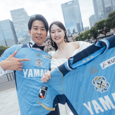 丸の内のビル街を背に、応援するサッカーチームのユニフォームを掲げて笑う新郎新婦。ふたりの趣味を取り入れたおしゃれな結婚写真