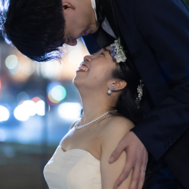街の灯りをぼかした背景で顔を寄せ合う新郎新婦。夜の東京駅周辺で撮るロマンチックな前撮り