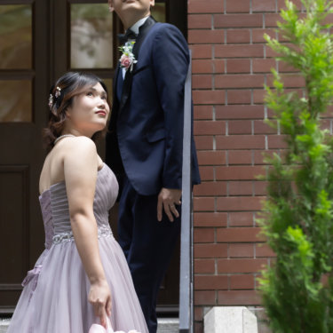 見上げるようにポーズをとる新郎新婦。赤レンガの壁と木製のアーチ扉が印象的なロケーションフォト