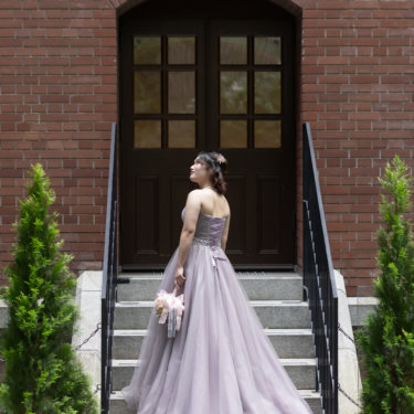 赤レンガの洋館の階段でドレスの裾を大きく広げ、振り返る新婦。くすみパープルのカラードレスで撮る丸の内の前撮り