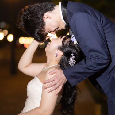 街灯の下で花嫁を抱き寄せ、笑い合う新郎新婦のクローズアップ。ネイビータキシードで撮る夜の東京駅前の結婚写真