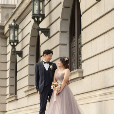 並んだガス灯とアーチ窓が続く石造りの洋館の前で見つめ合う新郎新婦。くすみピンクのカラードレスが映える丸の内のロケーションフォト