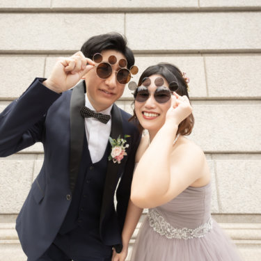 おそろいの変わり種サングラスをかけてポーズをとる新郎新婦。石造りの階段を背にした遊び心のある前撮りスナップ