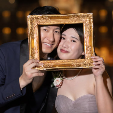 金色の額縁から顔を出して並ぶ新郎新婦。東京駅丸の内駅舎のライトアップをぼかした、遊び心のあるフォトウェディング