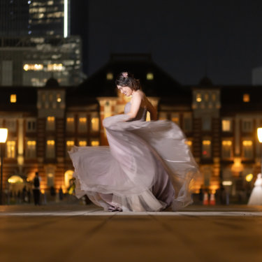 ドレスの裾を大きく翻してターンする新婦。東京駅丸の内駅舎のライトアップを背にした動きのあるフォトウェディング