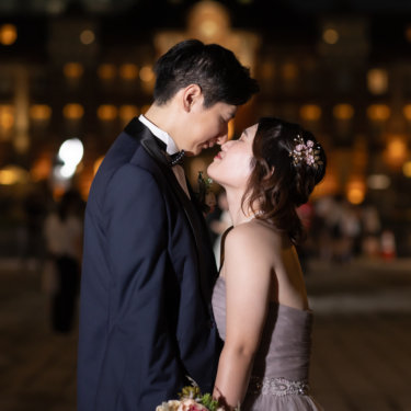 東京駅丸の内駅舎のライトアップを背に、くすみカラーのドレスの新婦とネイビータキシードの新郎が見つめ合う縦構図