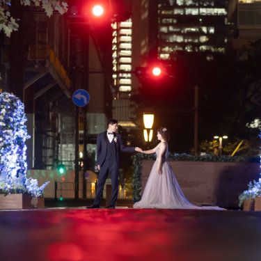 青いイルミネーションが灯る丸の内仲通りで手を取り合う新郎新婦。くすみピンクのカラードレスで撮る夜のロケーションフォト