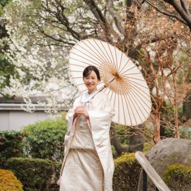 白い和傘を差して石橋に立つ白い色打掛の花嫁を縦位置でとらえた一枚。目白庭園で撮る和装前撮りのブライダルポートレート