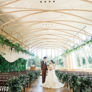 木造アーチ天井と緑に包まれたナチュラルなチャペルで、バージンロードに立つ新郎新婦のフォトウェディング