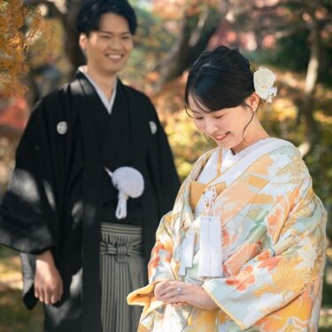 平成庭園の紅葉を背景に微笑む、水色地に花柄の色打掛の花嫁と黒紋付袴の新郎の和装前撮り