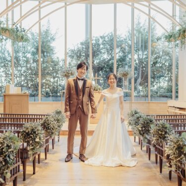 緑に囲まれたアーチ窓のチャペルで、バージンロードに手をつないで立つ新郎新婦のチャペルフォト