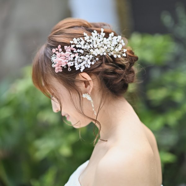 白いパールと淡いピンクの生花をあしらったヘアアレンジ、うつむいて微笑む新婦。