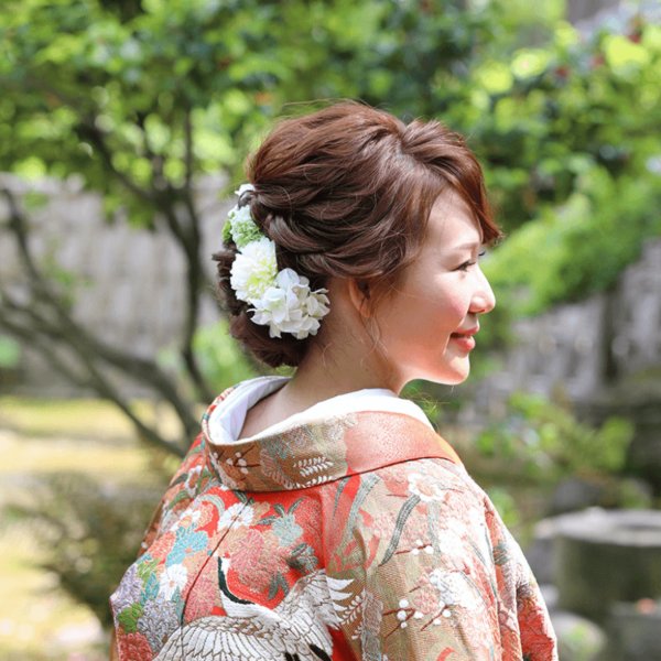 白い生花の髪飾りをつけ、色打掛姿で振り返る新婦の横顔。