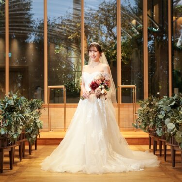 木造アーチのチャペルの窓を背景に、ブーケを持って佇むウェディングドレスの花嫁のチャペルフォト