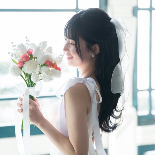 白とピンクのチューリップのブーケに顔を寄せる新婦、白いリボンの髪飾りとイヤーカフ。