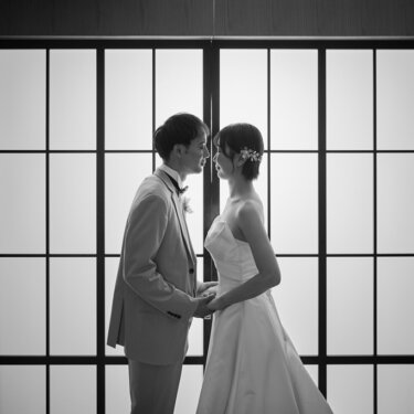 障子の光を背に手を取り合う、スーツの新郎とウェディングドレスの花嫁をモノクロで写したスタジオフォト