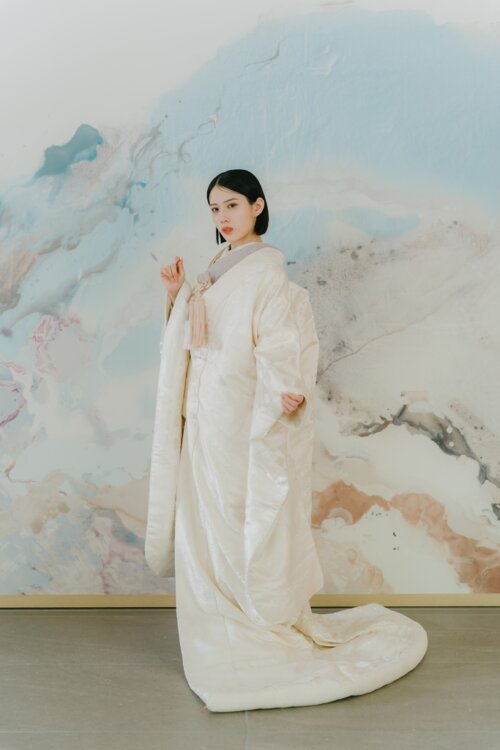 水彩画のようなアートウォールの前に立ち、長い裾を引いた白無垢の花嫁の全身ショット。和装フォトウェディングの衣装選びに役立つ白無垢AS104