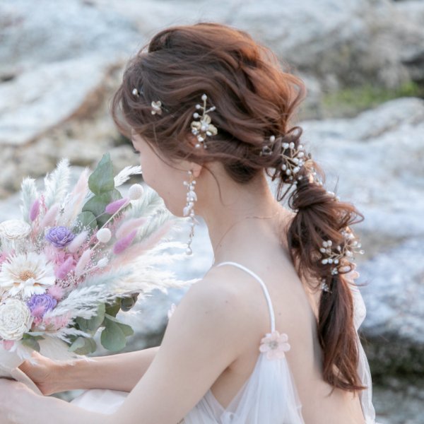 岩場を背景に、パールをあしらったヘアアレンジの後ろ姿、パープルとホワイトのドライフラワーブーケ。