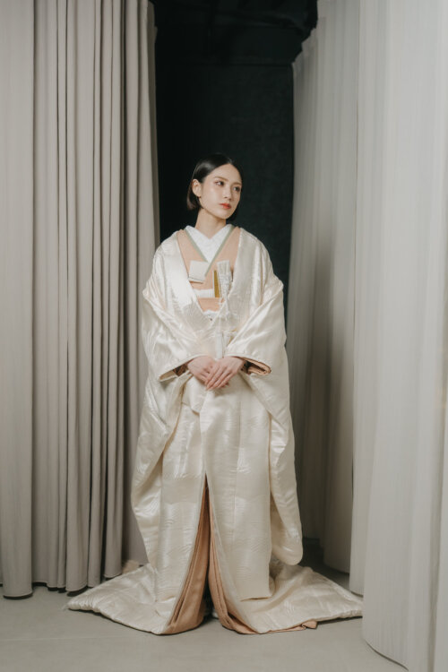 カーテンを背に両手を重ねて正面に立つ白無垢の花嫁。裾を広げた全身の立ち姿が上品な、スタジオでの結婚写真