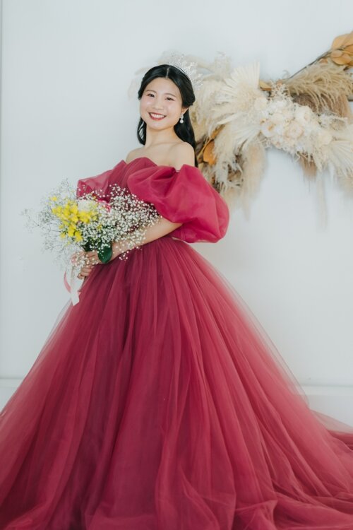 パンパスグラスの飾りの前でブーケを持って笑うピンクのカラードレスの花嫁を縦位置でとらえた一枚。東京駅店のスタジオで撮る洋装前撮りのカラードレスカット