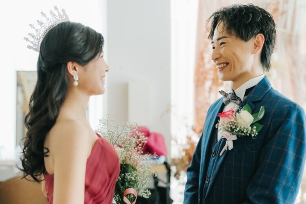 ティアラを付けた赤いカラードレスの花嫁と向かい合って笑うネイビーのスーツの新郎の横顔。東京駅店のスタジオで撮る洋装前撮り