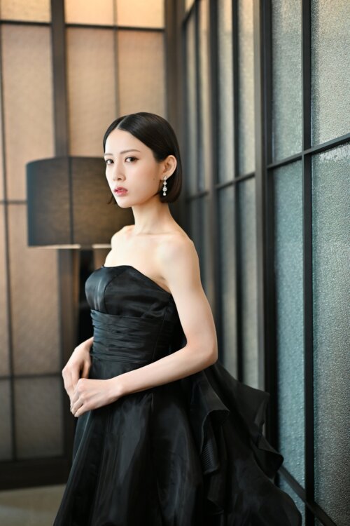 ガラスの格子戸の前で黒いフリルのカラードレスを着て立つ花嫁を縦位置でとらえた一枚。東京駅店のスタジオで撮る洋装前撮りのブラックドレス
