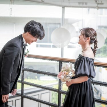 吹き抜けの手すりの前で、黒いオフショルダードレスの花嫁と笑い合うタキシードの新郎。南青山ラウンジスタジオのカラードレス前撮り