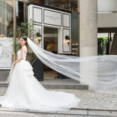 WEDDING AVENUEのラウンジ入口前でロングベールをなびかせて振り返る花嫁。石畳で撮るウェディングフォト